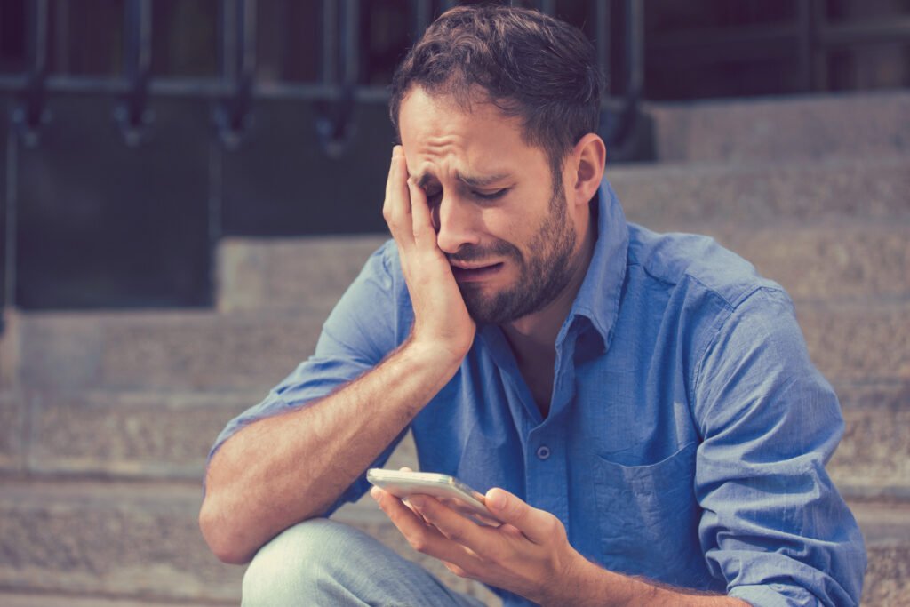 A very upset man is looking at the message on his mobile phone when he finds out that his girlfriend has broken up with him.