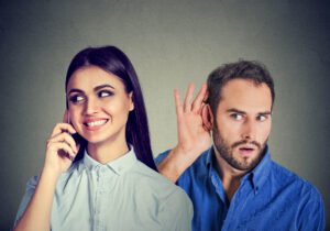 Curious man secretly listening to a happy woman talking on mobile phone.